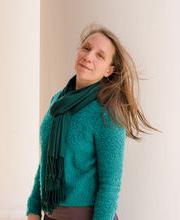 Jennifer Schoonover smiling standing next to a large white column on the portico of Boyden Hall with long straight light brown hair wearing a teal blue sweater and green scarf